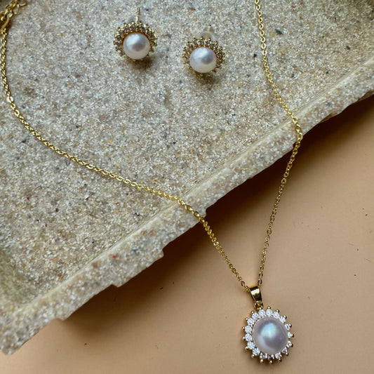 Elegant and classic, this jewelry set includes a gold necklace with a luminous pearl pendant surrounded by a delicate halo of crystals, and coordinating stud earrings. A perfect gift, this set showcases the beauty of pearls and sparkling accents.
