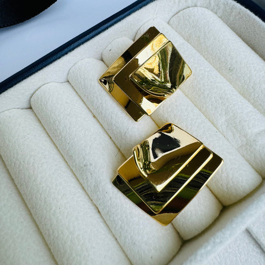 Bold geometric gold earrings with a layered square design, exuding modern elegance, displayed in a plush jewelry box