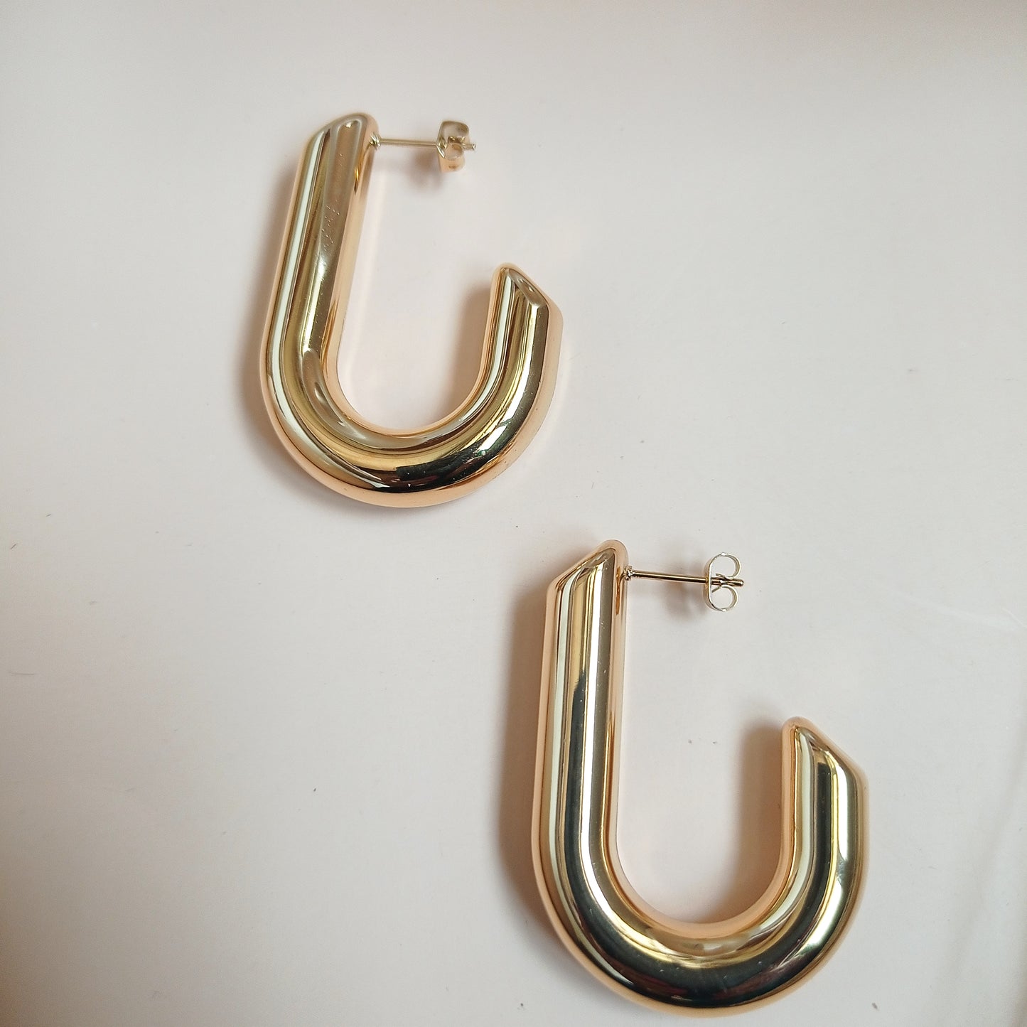 Minimalist gold U-shaped hoop earrings, exuding modern elegance, set against a neutral-toned backdrop with ceramic accents