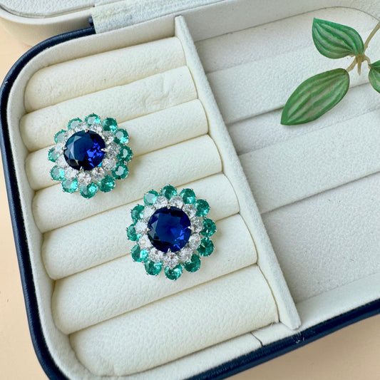 Fashionable earrings with a geometric design and a bold green blue accent, stored in a protective case.
