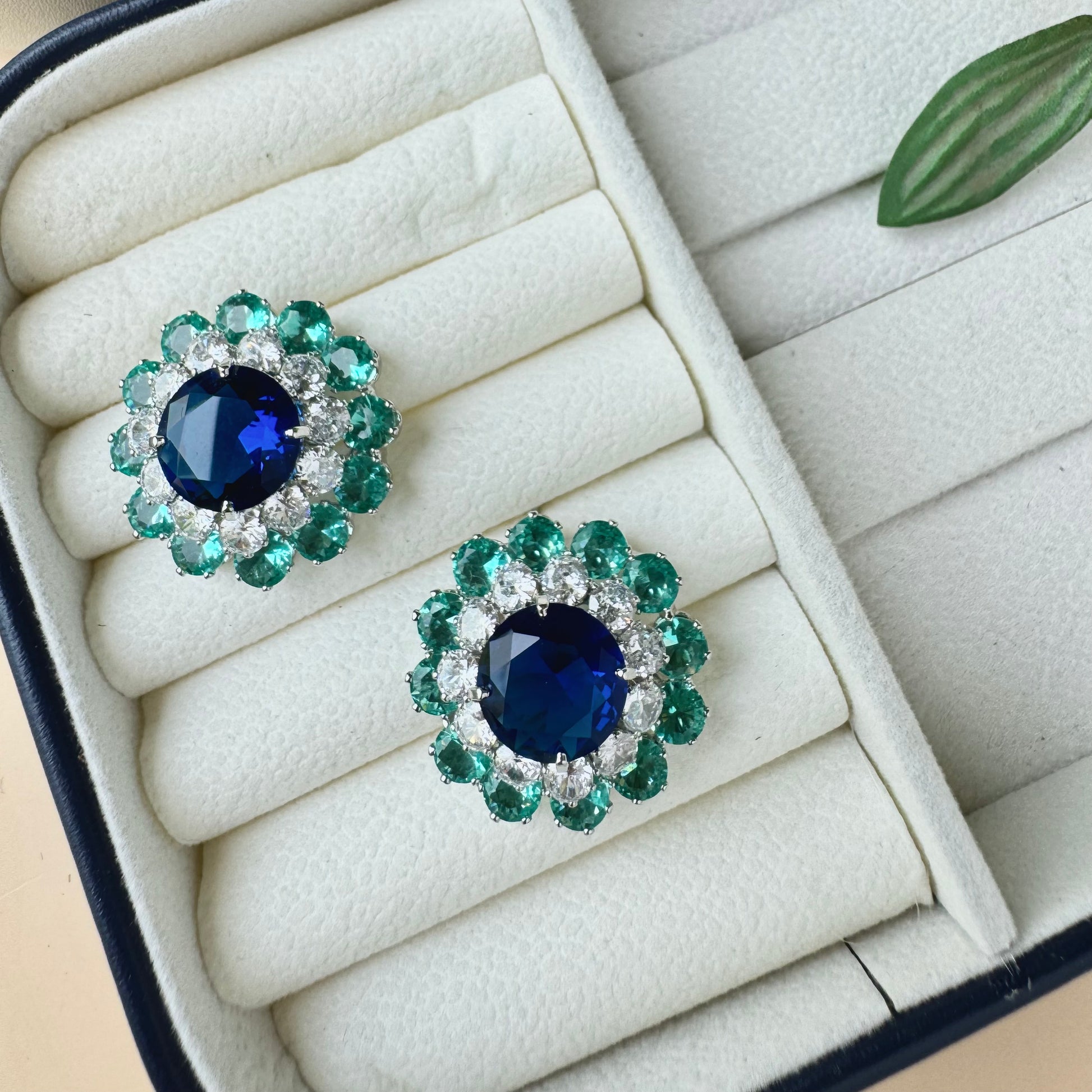 Fashionable earrings with a geometric design and a bold green blue accent, stored in a protective case.