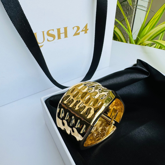 gold-toned, flexible tubular bracelet on a white display.